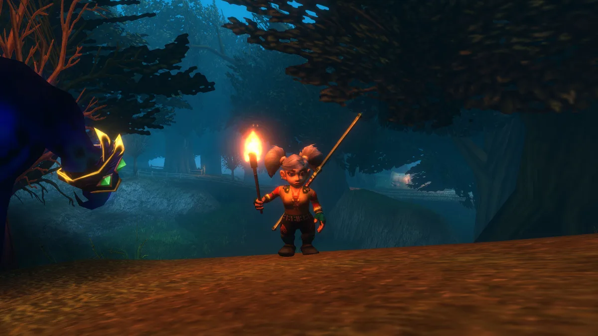 A gnome holds a burning torch in the misty, dark woods of Duskwood, its flame lighting her face and the ground around her